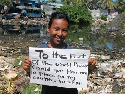 Foto eines lächelnden Insulaner-Mädchens mit Schild „An den Rest der Welt: Bereitet Ihr bitte schon mal einen Platz für mein Land vor?“